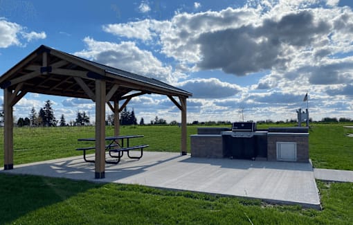 A picnic pavilion with a grill and picnic table is set up in a grassy field.