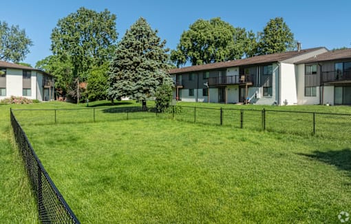 A grassy field with a fence and apartment buildings in the background.