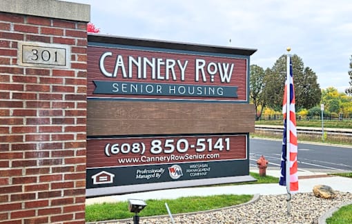 A sign for Cannery Row Senior Housing is displayed in front of a brick wall.