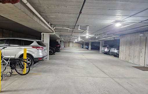A parking garage with a white car parked on the left and a bike on a yellow rack.