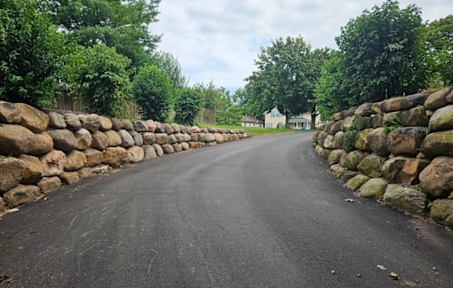 A road with a stone wall on one side and trees on the other.
