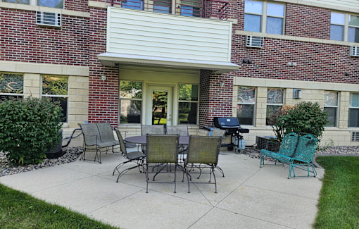 A patio with a table and chairs in front of a brick building.