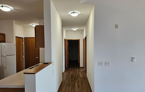 A long hallway with a refrigerator on the left and a door at the end.