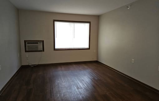 an empty room with a window and hardwood floors