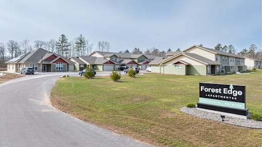 A sign for Forest Edge Apartments is in the foreground of a road with houses in the background.