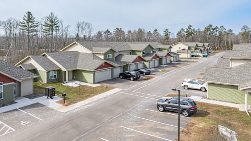 A parking lot with cars and houses in the background.