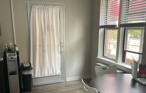 A room with a table, chairs, and a window with red blinds.