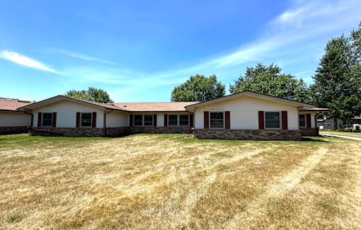 A house with a red roof and white walls with a lawn in front.