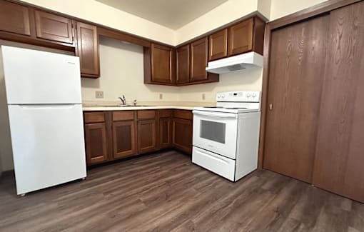 A white refrigerator stands in a kitchen with wooden cabinets and a white stove.