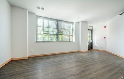 A large empty room with wooden floors and a window with blinds.