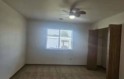 A room with a ceiling fan and a window with blinds.