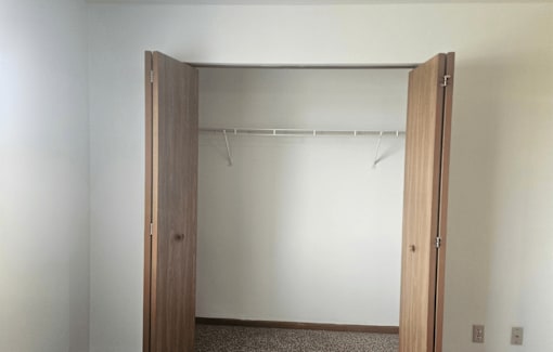 A white wall with a wooden closet door open.