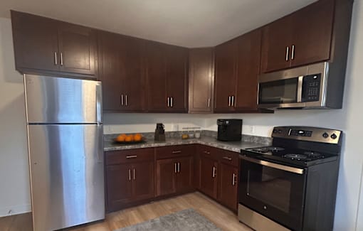 A kitchen with a stainless steel refrigerator, black oven, and wooden cabinets.