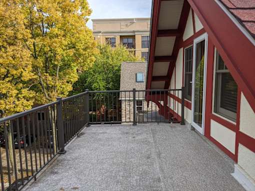 A balcony with a black railing and a red and white building in the background.