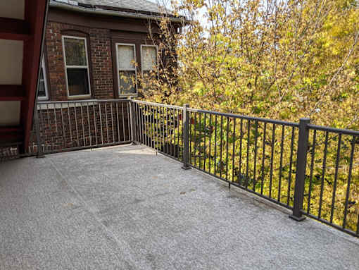 A patio with a black railing and a grey concrete floor.