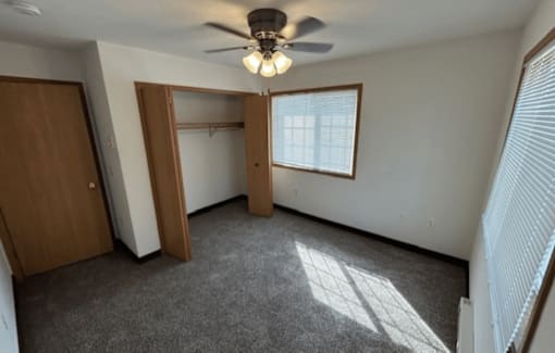 A room with a ceiling fan and a window with blinds.