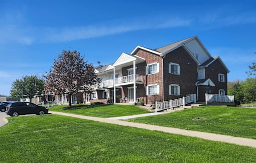 A large brick house with a white porch and a black car parked in front.
