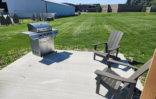 A BBQ grill is on a patio with two chairs.