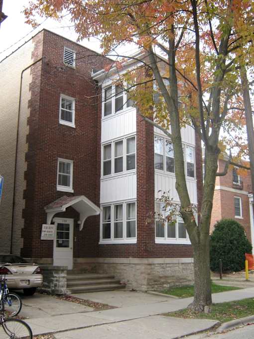 A tree with orange leaves stands in front of a red brick building.