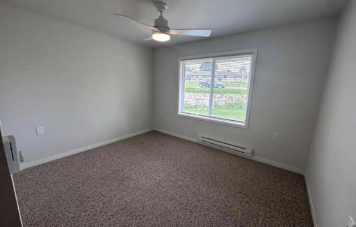 A room with a ceiling fan and a window overlooking a parking lot.