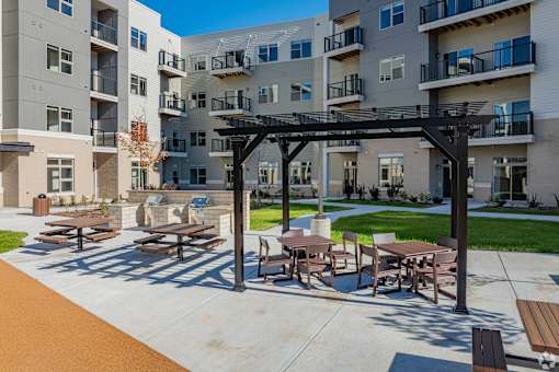 A patio with tables and chairs is in front of apartment buildings.