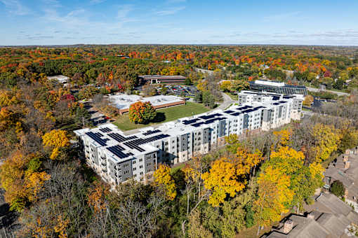 A large white building with a green roof surrounded by trees with orange and yellow leaves.