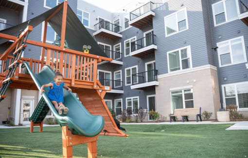 a young boy playing on a slide in front of an apartment complex