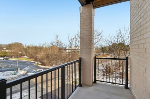 A balcony with a black railing and a view of a parking lot and trees.