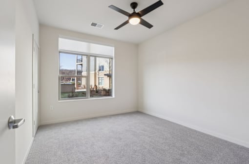 A room with a ceiling fan and a large window overlooking a cityscape.