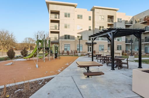 A playground area with a slide and picnic tables in front of apartment buildings.