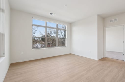 Empty room with a large window and wooden flooring.
