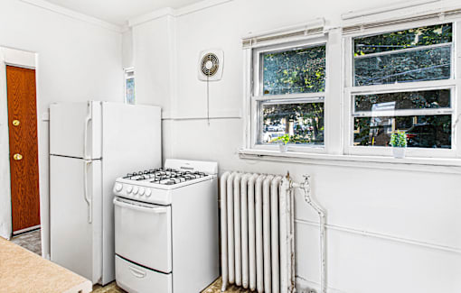A white kitchen with a stove, refrigerator, and radiator.