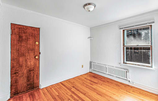 A room with a wooden door and a window with a radiator under the window.