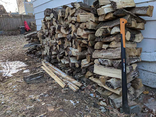 A pile of wood is stacked against a white house.