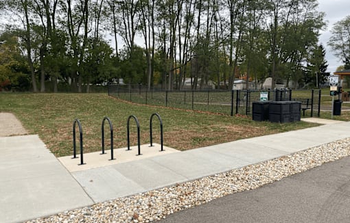 A park with a fence, trees, and a trash can.