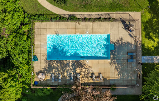 An aerial view of a rectangular swimming pool surrounded by a concrete patio and a grassy area.