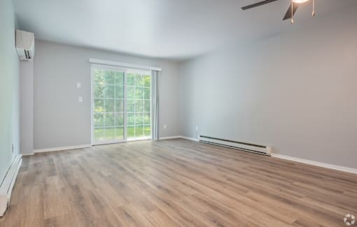 A room with wooden flooring and a sliding glass door leading to a balcony.