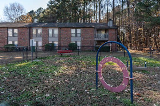 A playground with a red and blue swing set in front of a brick building.