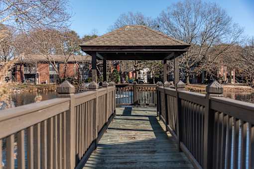 A wooden gazebo sits on a wooden bridge over a body of water.