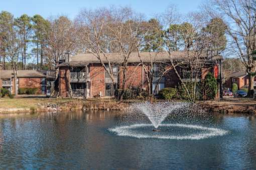 A fountain in the middle of a pond in front of a building.