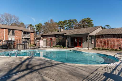 A swimming pool in front of a brick building with a red door.
