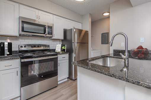A kitchen with a stove, microwave, refrigerator, and sink.
