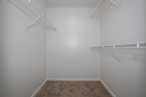 a walk in closet in a bedroom with white walls and carpet