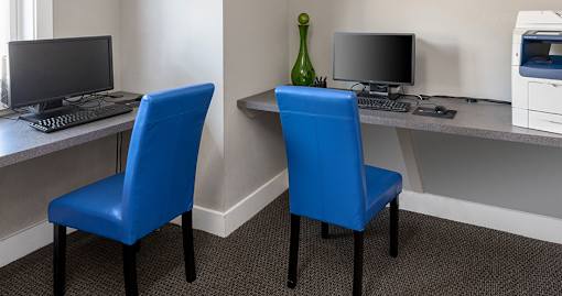 Two blue chairs are placed in front of a desk with a computer and a monitor.