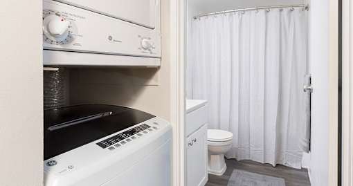 A white washing machine is in a small bathroom with a toilet and a shower curtain.