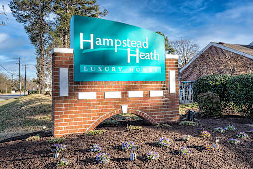 A sign for Hampstead Heath Luxury Homes is displayed in front of a brick wall.