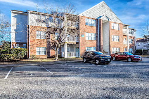 Two cars are parked in a parking lot in front of a brick apartment building.