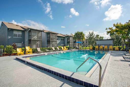 A swimming pool surrounded by yellow chairs and apartment buildings.