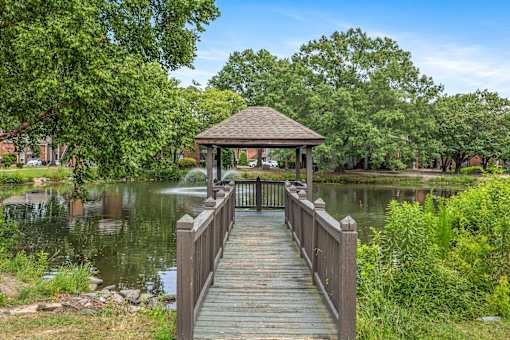 A wooden pier leads to a gazebo over a lake surrounded by trees.