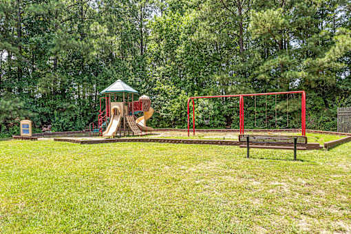 A playground with a red swing set and a green canopy.